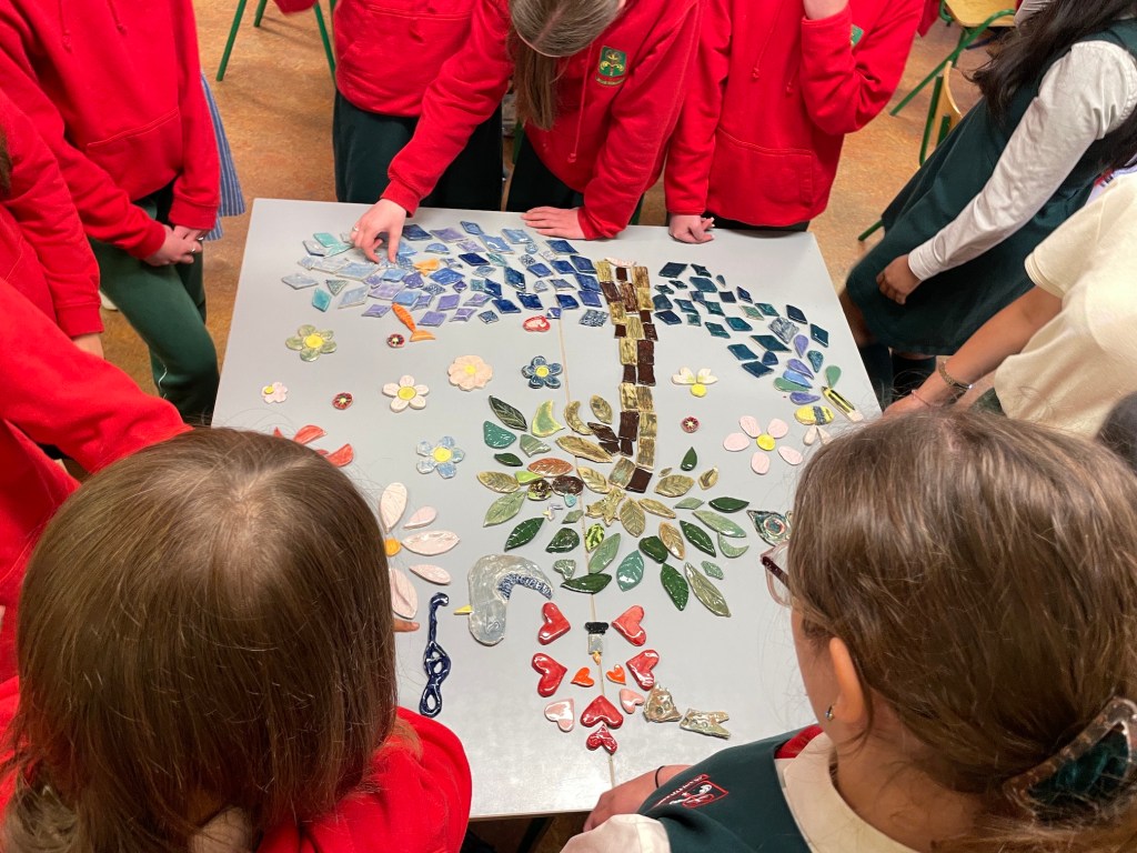 pieces of ceramic arranged inot an image of a tree surrounded by young students