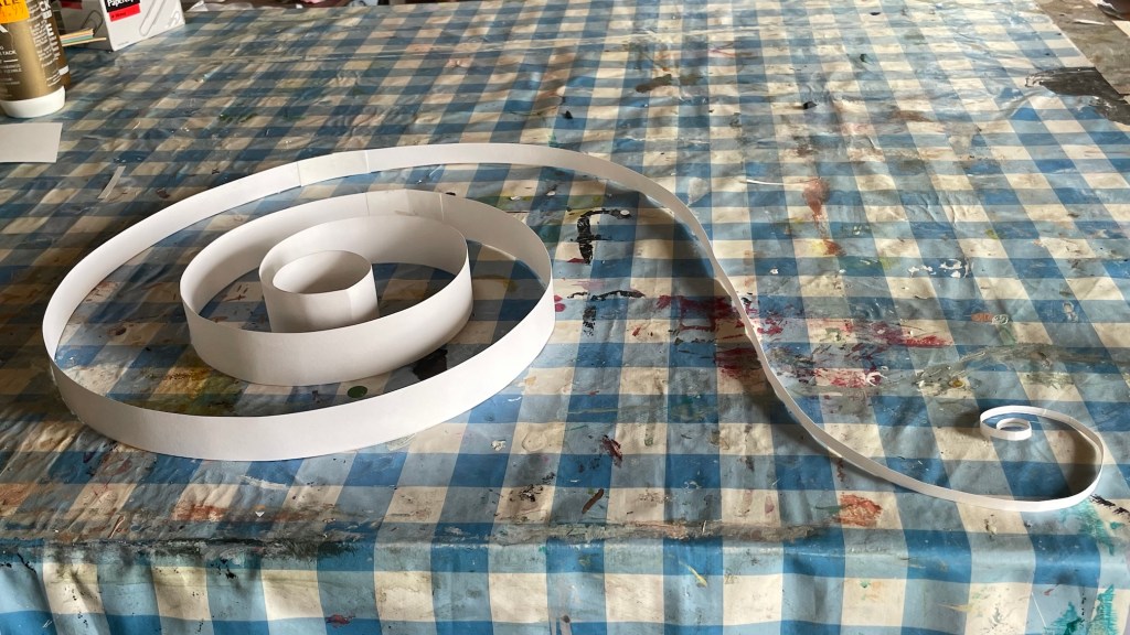 a model for a sculpture made of a spiral of coiled white paper on a blue and hite check pattern table top