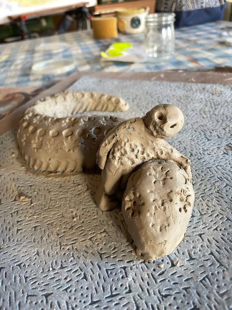 a clay model of a humanoid creature hugging a lizard's back